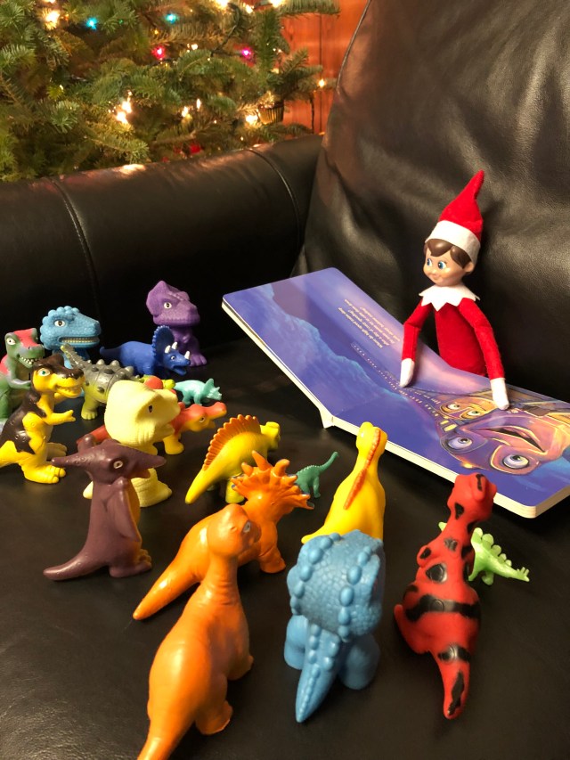 Elf on the Shelf reading to his dino friends